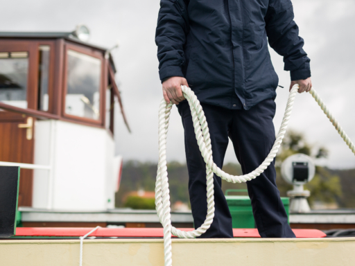 Anlegen Ein Nautik-Mitarbeiter steht auf einem Schiff und hält eine Leine in der Hand, die beim Anlegen und Festmachen des Schiffs gebraucht wird.