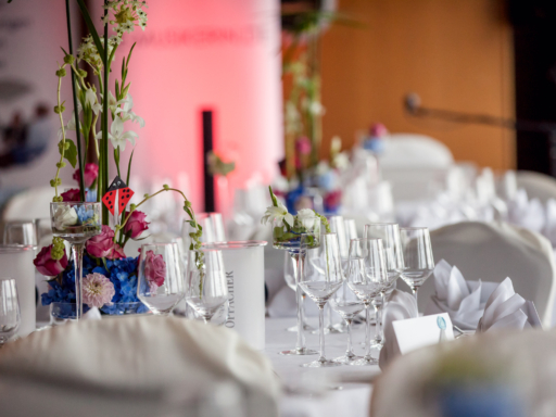 Glasses are ready on a table, napkins are laid out, and a floral arrangement with pink roses decorates the table.