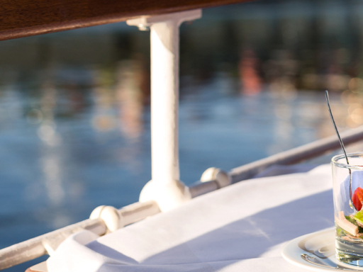 On a table on a steamer there is an appetizer in a glass and a glass of wine.