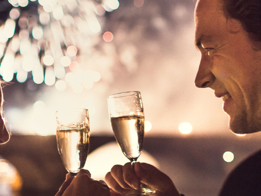 Couple toasting with champagne, in the background it is dark, only fireworks can be seen.