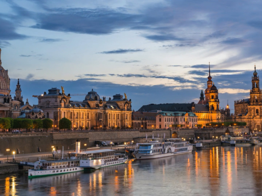Ship Operation Plan The silhouette of Dresden's Old Town at dusk, overlooking the Terrassenufer, where several steamers and saloon boats are moored. The lights of the Old Town are reflected in the waters of the Elbe.