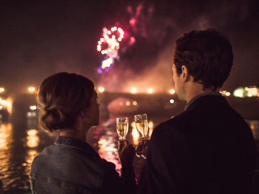 IMG_5512 Ein Mann und eine Frau mit zwei Sektgläsern sehen sich ein Feuerwerk über der nächtlichen Elbe an.