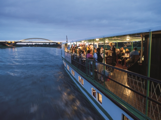 Abendfahrt auf einem beleuchteten Dampfer in der Dämmerung. Die beleuchtete Waldschlößchenbrücke ist im Hintergrund zu sehen.