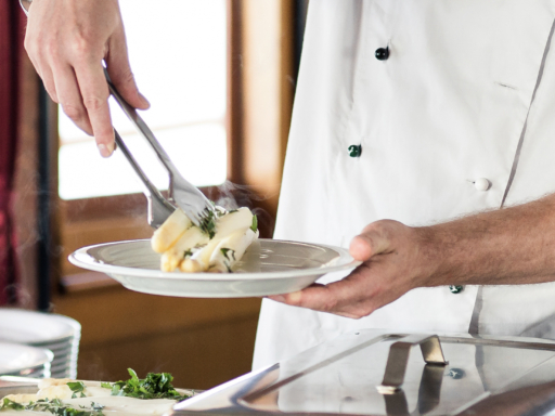 Teamleiter Gastro An einem Buffett legt ein Gastromitarbeiter mehrere Stangen weißen Spargel auf einen Teller.