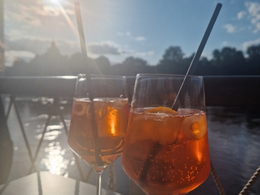 Aperol Sprizz Zwei mit Aperol gefüllte Gläser stehen auf dem Sonnendeck auf einem Tisch. Im Hintergrund scheint die Sonne.